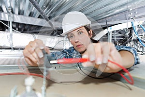 Female electrician installing electric device in ceiling