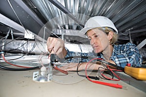 female electrician installing electric device in ceiling