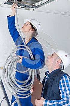 Female electrician installing wires in ceiling