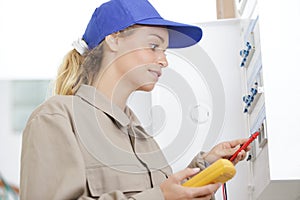 Female electrician using multimeter on circuit breaker cabinet