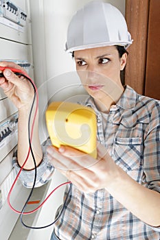 female electrician using multimeter to test electrical cabinet