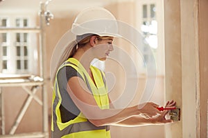 Female Electrician Wearing Hard Hat Fitting Light Switch At New Build Property