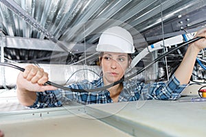 Female electrician wiring in building ceiling