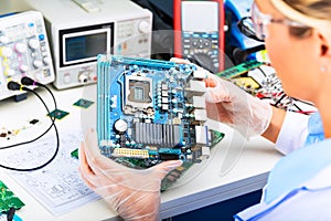 Female electronic engineer examining computer motherboard in lab