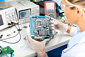 Female electronic engineer examining computer motherboard in lab