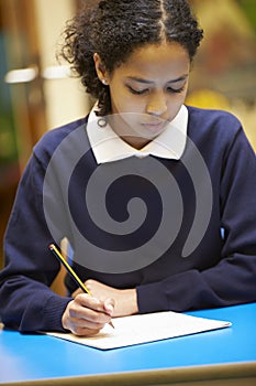 Female Elementary School Pupil Writing Book In Classroom