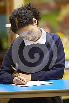 Female Elementary School Pupil Writing Book In Classroom