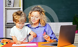 Female elementary school teacher helping little boy with writing lesson in classroom at school. Young female teacher