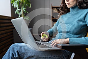 Female employee exercising with hand expander while working on laptop computer in office