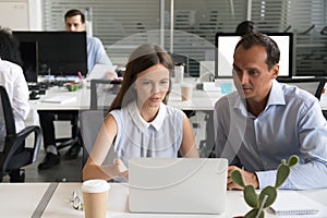 Female employee explaining computer task to male coworker workin