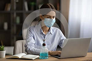 Female employee in facial mask work on laptop online