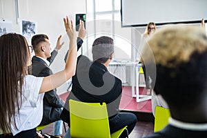Female employee raise hand asking question to businesswoman making flipchart presentation. Young woman answering during