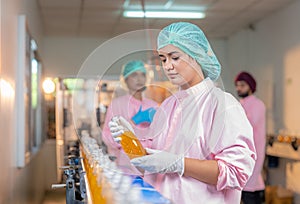 Female employee worker in uniform checking quality of fruit juice drinks bottle in production line food and beverage factory