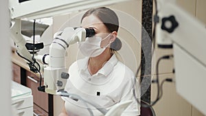 A female endodontist is treating canals under the microscope.