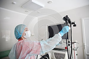 A female endoscopist surgeon in a protective suit, cap, mask and gloves picks up an endoscope before starting procedure