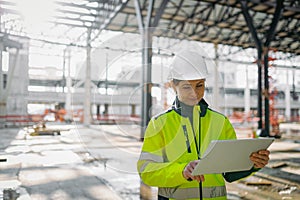 Female engineer checking building documentation on clipboard at construction site.