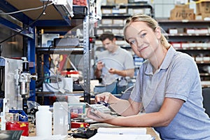 Portrait Of Female Engineer In Factory Measuring Component At Work Bench Using Micrometer