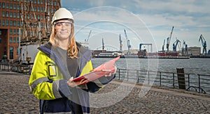 Female engineer holding a clipboard in front of hamburg port background
