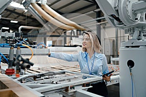 Female engineer in modern industrial factory, checking robotic arm, controling process and manufacturing equipment or