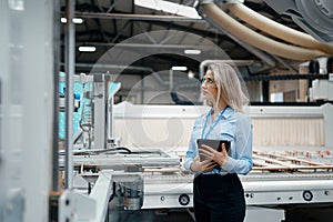 Female engineer in modern industrial factory, checking robotic arm, controling process and manufacturing equipment or