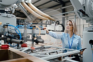 Female engineer in modern industrial factory, checking robotic arm, controling process and manufacturing equipment or