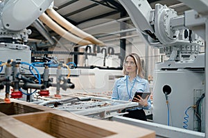 Female engineer in modern industrial factory, checking robotic arm, controling process and manufacturing equipment or