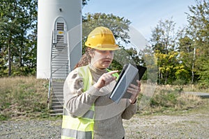 Female engineer in a safety vest standing next to a windmill