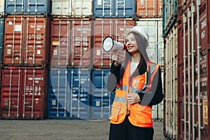 Female engineer speaking into a megaphone while standing in an industrial warehouse or terminal with shipping containers