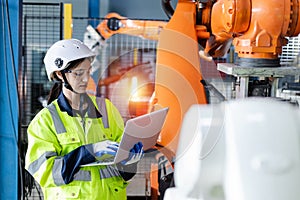 Female engineer using laptop control and checking system robot arm automate. robotic automation in line production at industrial.