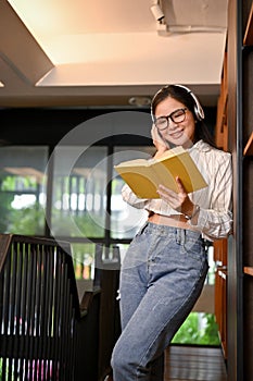 Female enjoys listening to music through headphones while looking up information on a book