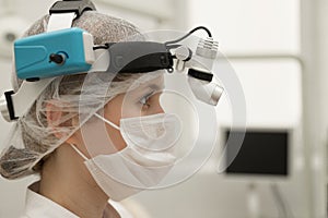 A female ENT doctor in a white coat and a mask is in the modern office of an ENT hospital, close-up