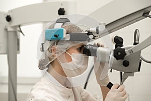 A female ENT doctor in a white coat and a mask is in the modern office of an ENT hospital, look into slit lamp
