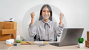 Female entrepreneur is celebrating success with arms up after checking customer order on laptop before packing