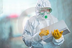 Female epidemiologist in protective clothing reading research report in quarantine