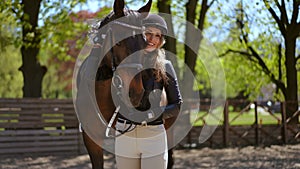 Female equestrian adjusting horse bridle turning looking at camera with toothy smile. Portrait of professional confident