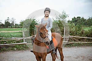 Female equestrian smiling while riding horse and holding reins