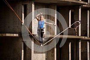 Female equilibrist standing with one arm raised and other to the right on the slackline rope