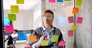 Female executive looking on sticky note on glass wall 4k