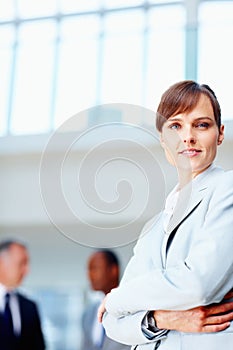 Female executive standing casually with colleagues in background. Business woman smiling while standing with arms folded