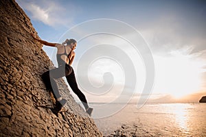 Female extreme climber conquers steep rock against the sunset over river.
