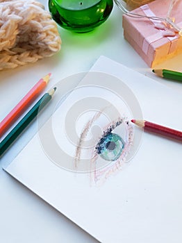 Female eye drawn colorful pensils surrounded with cozy objects