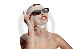 Female face bandaged with medical bandages and sunglasses with human emotions. Making beauty, modifying face to make
