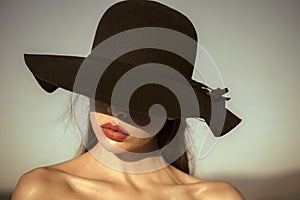 Female Face. Issues affecting girls. Portrait of elegant beautiful woman in a black wide hat on blue sky background.