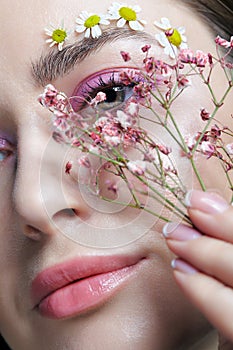 Female face with pink makeup. Woman with Gypsophila flowers in hand near face. Brows are decorated by small chamomile flowers