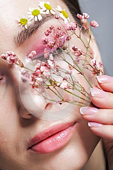 Female face with pink makeup. Woman with Gypsophila flowers in hand near face. Brows are decorated by small chamomile flowers