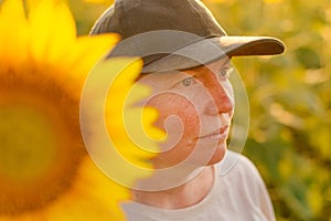 Female farm worker with trucker's hat in blooming sunflower field. Agriculture and farming concept