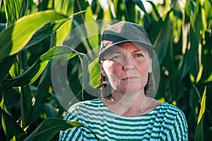 Female farmer and agronomist posing in green corn crop agricultural field and looking into distance while contemplating