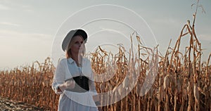 A female farmer in a dress and hat walks along the fields of ripe corn.