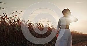 A female farmer in a dress walks among the fields of corn