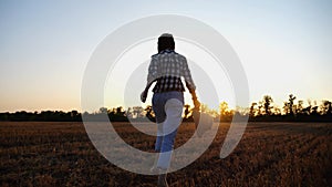 Female farmer running through the barley plantation at sunset. Agronomist jogging among wheat meadow at dusk. Beautiful